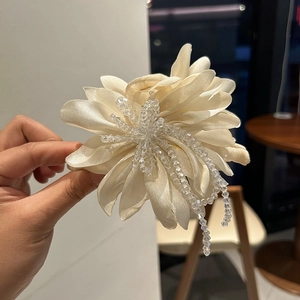 Detailed close-up of large cream fabric flower hair claw with crystal beaded tassels