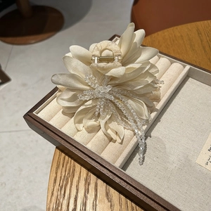 Detail of cream fabric floral hair claw with hanging beaded tassels on wooden tray