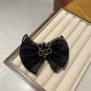 Detail of black mesh bow hair clip with central rhinestone flower on a velvet tray