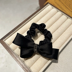 Detail of a black satin bow hair tie with micro-set black rhinestones in a wooden box