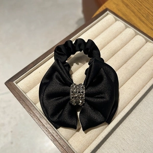 Close-up of black satin bow hair tie with dark shimmering rhinestone center on display