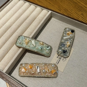 Detailed close-up of shell pearl hair clips with rhinestones in a beige velvet box