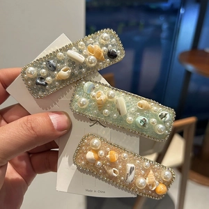 Close-up of three pearl and shell hair clips with rhinestones on a display card