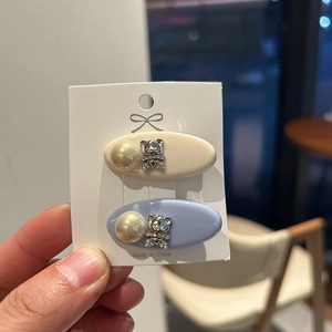 Detail of two resin hair clips with pearl and rhinestone bear on white card