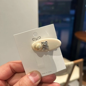 Detail view of oval beige resin hair clip with pearl and rhinestone bear on card