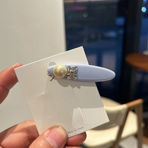 Detail of blue acetate hair clip with pearl and rhinestone bear on white card