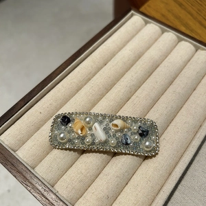 Close-up of pearl shell hair clip with rhinestones and beads on beige jewelry box