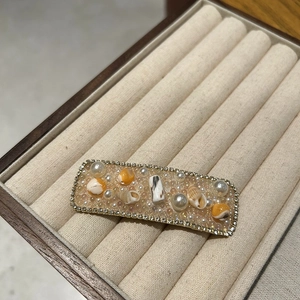 Macro view of a rectangular hair clip featuring inlaid pearls, seashells and crystals