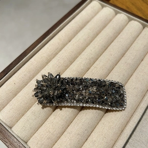 Detailed close-up of dark grey crystal hair clip with sparkling rhinestone floral ornament