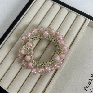 Detail of pink pearlescent beads on a golden elastic woven hair tie in a display tray
