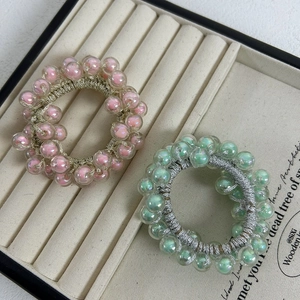 Set of two colorful beaded hair ties with iridescent beads on a beige velvet tray