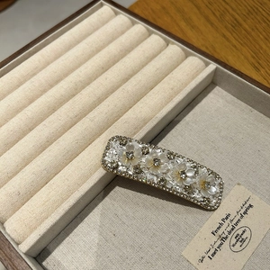 Detail of floral hair clip with shell flowers and rhinestones on beige velvet base