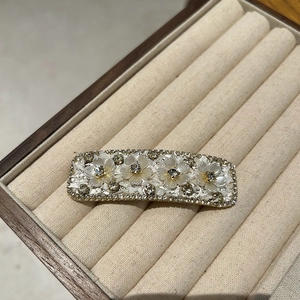 Close-up of floral hair clip with rhinestones and beige resin flowers on a velvet tray