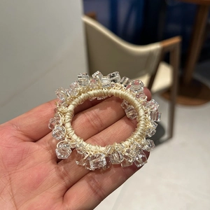 Dettaglio di un elastico per capelli con perline di cristallo trasparente e corda beige