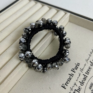 Elastic black hair tie with faceted silver crystal beads on a beige jewelry tray