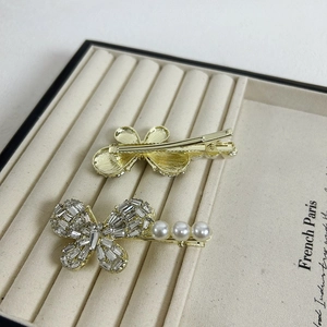 Elegant gold bow hair clip with sparkling zircons and pearls on a beige velvet tray