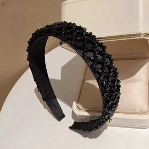 Gros plan d'un serre-tête large orné de perles noires facettées sur un coffret cadeau