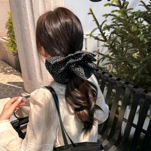 Polka dot oversized bow scrunchie shown on a ponytail with a natural outdoor background