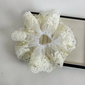 Détail d'un chouchou en dentelle blanche orné de perles crème et de motifs floraux brodés