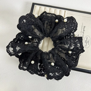 Détail d'un chouchou en dentelle noire avec bords ondulés et perles blanches