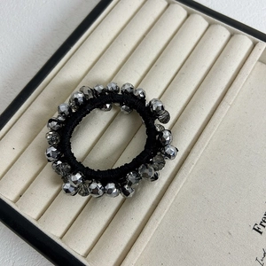 Close-up of silver-gray faceted beads on a black elastic hair tie in a jewelry tray