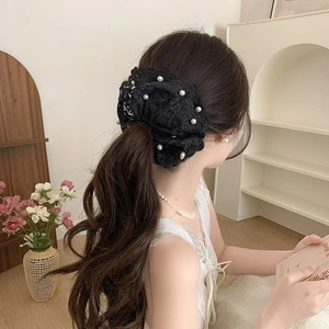 Détail d'un chouchou en dentelle noire avec perles porté sur une queue de cheval