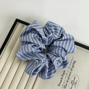 Close-up of a blue and white striped fabric hair scrunchie on a beige jewelry tray