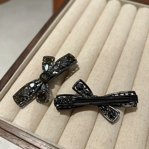 Detail view of two bow-shaped gunmetal hair clips with sparkling dark grey rhinestones