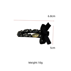 Detail showing a 6.8cm black ribbon bow hair clip with luxury rhinestones and Lucky charm