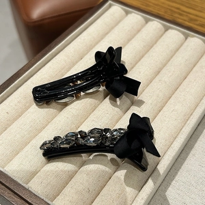 Detail showing two luxury duckbill hair clips with rhinestones and black silk bows