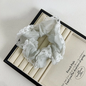 Close-up of white lace trim on shiny silver organza scrunchie displayed on a tray