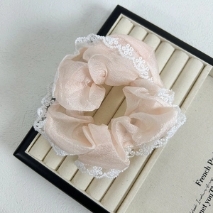 Detail of light peach organza scrunchie with white floral lace trim in a display case