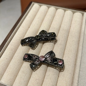 Detail of luxury rhinestone bow hair clips in pink and green on beige velvet tray