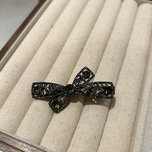 Detailed macro view of a dark grey rhinestone bow hair clip on a soft velvet tray
