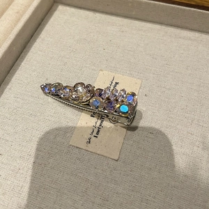 Detail of floral rhinestone hair clip with purple stones and a pearl on beige linen