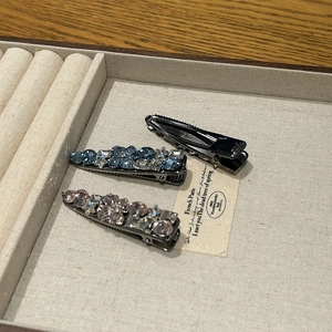 Detailed view of vintage crystal duckbill hair clip set on a beige jewelry display tray