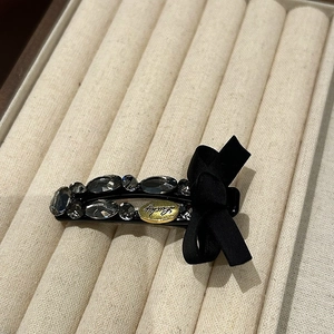 Detail of black ribbon bow hair clip with smoky grey rhinestones and Lucky gold charm