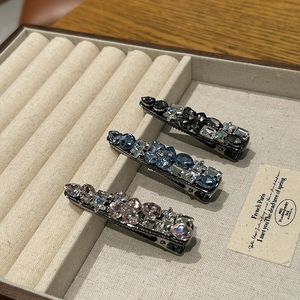 Detailed macro view of three crystal-encrusted duckbill hair clips on a velvet tray