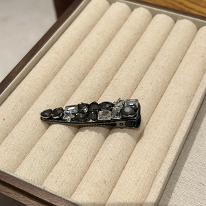 Detailed close-up of a luxury black hair clip with diverse crystal shapes on velvet tray