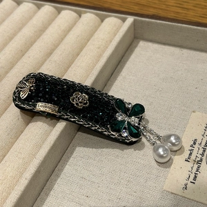 Detailed close-up of emerald floral hair clip with gold bee and dangling pearl charms