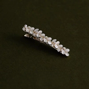 Eleganter goldener Haarclip mit Opal-Katzenaugensteinen und Perlen auf grünem Hintergrund