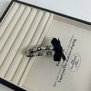 Detailed close-up of a black satin bow hair clip adorned with sparkling square rhinestones