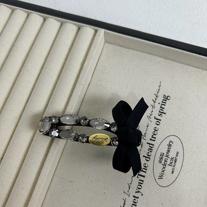 Detail of luxury ribbon bow hair clip featuring gray crystals and Lucky engraved metal plate