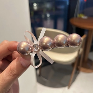 Détail de la pince à perles champagne avec nœud en ruban rose et strass brillant