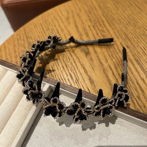 Detail of black floral crystal headband with small hair clips on a warm wooden surface