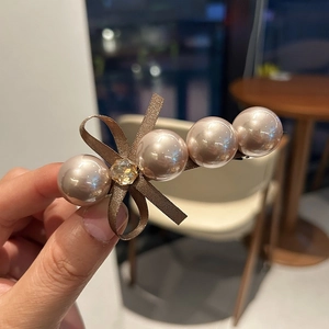 Détail d'une barrette à perles champagne avec nœud en ruban marron et strass jaune