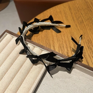 Detail of elegant pearl headband with black satin bows on a velvet display tray