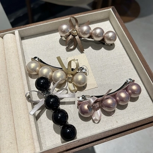 Détail de quatre barrettes en perles avec nœuds en rose, crème, noir et or champagne
