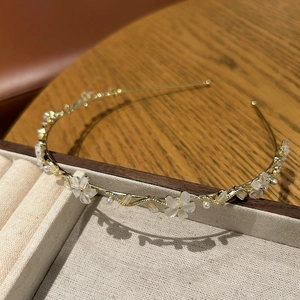 Détail d'un serre-tête doré avec fleurs blanches mates et perles sur une boîte à bijoux