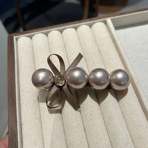 Détail de perles champagne et nœud en soie marron avec strass sur une pince à cheveux